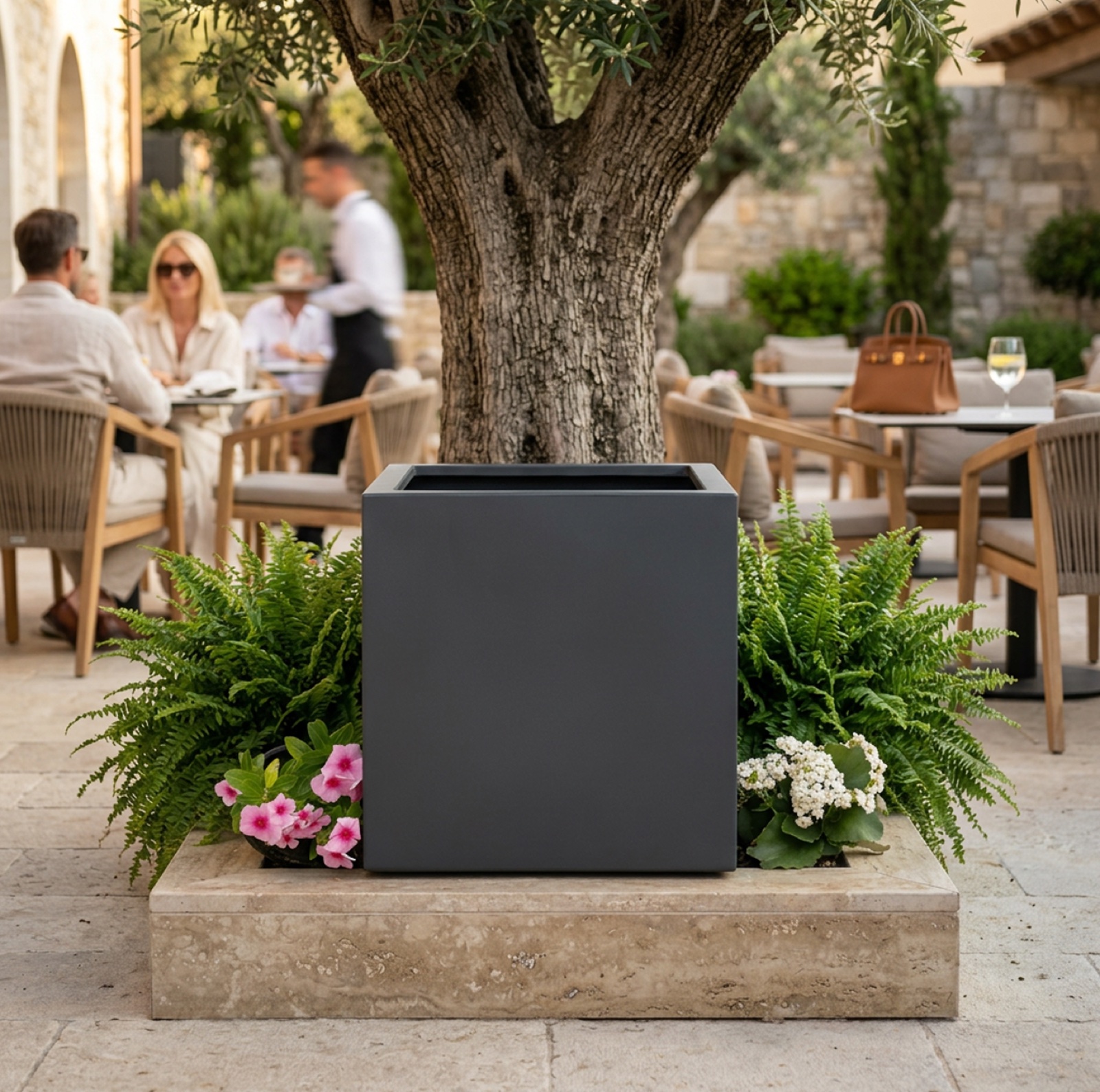 Vaso cubico in resina antracite con felci e fiori su base in travertino in area lounge